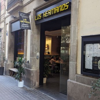 Los Hermanos’ stone-framed entrance and yellow sign at Carrer de Villarroel, 28